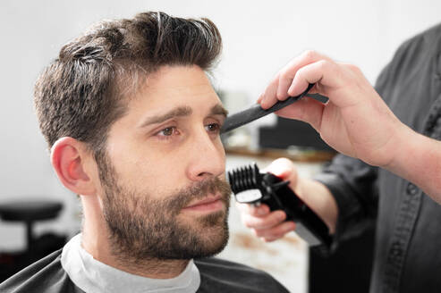 Man barber cutting hair of male client with clipper at barber shop. Hairstyling process. High quality photography. Man barber cutting hair of male client with clipper at barber shop. Hairstyling process. - INGF12845