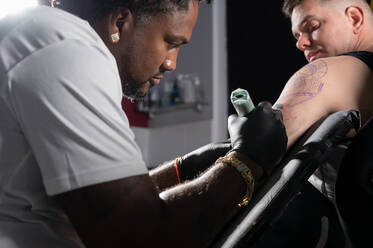 Professional African American tattoo artist makes a tattoo on client arm. High quality photography.. Professional African American tattoo artist makes a tattoo on client arm - INGF12849