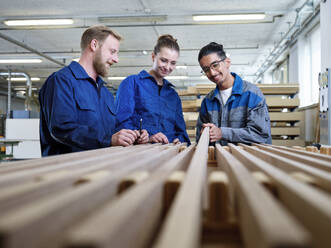 Smiling trainees looking at plank in factory - CVF02525