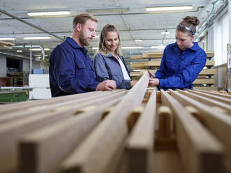 Trainee with carpenters examining wooden plank in workshop - CVF02538