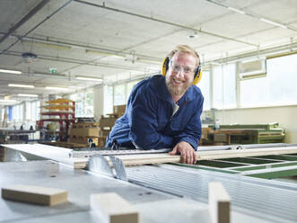 Lächelnder Schreiner in Arbeitsschutzkleidung in einer Fabrik - CVF02539