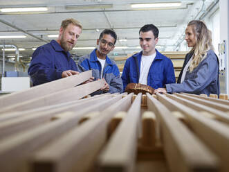 Zimmermann hält Holzbrett und erklärt Auszubildenden in der Fabrik - CVF02546