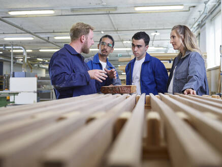 Carpenter explaining trainees over wooden planks in factory - CVF02550