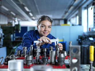 Lächelnder Metallarbeiter bei der Messung einer CNC-Maschine mit einem Messschieber in einer Produktionsstätte - CVF02559