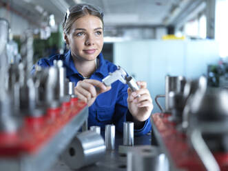 Contemplative metal worker with CNC tool and caliper in factory - CVF02574