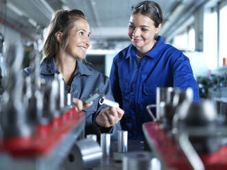 Lächelnder Industriearbeiter, der einem Auszubildenden in der Fabrik das Messen von CNC-Werkzeugen beibringt - CVF02576