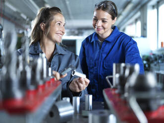 Smiling industry worker teaching trainee to measure CNC tool in factory - CVF02576