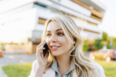 Blonde Frau, die im Freien mit einem Mobiltelefon spricht - MDOF01486