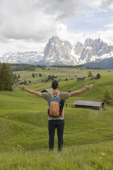 Explorer with arms outstretched looking at snow covered mountains standing on grass - MMPF00915