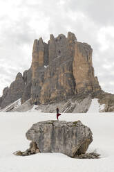 Man practicing yoga on rock surrounded by snow in front of mountain - MMPF00920