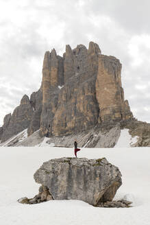 Mann übt Yoga auf einem Felsen, umgeben von Schnee, vor einem Berg - MMPF00920