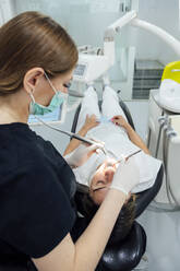 Dentist with surgical mask examining patient's teeth at clinic - PGF01647