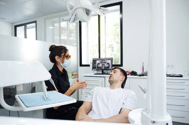 Dentist wearing surgical mask giving advice to patient in examination room - PGF01660