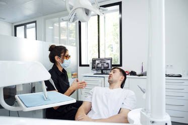 Zahnarzt mit chirurgischer Maske berät einen Patienten im Untersuchungsraum - PGF01660