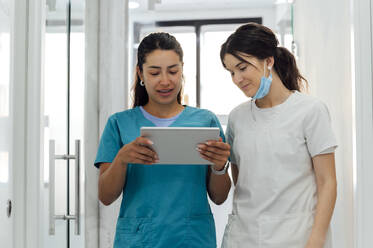 Smiling dentist using tablet PC by colleague in corridor - PGF01673