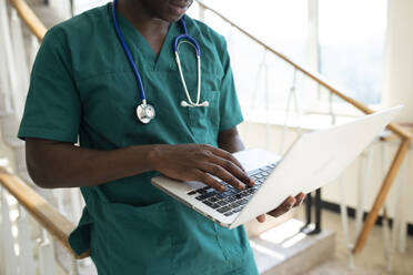 Medical student using laptop by staircase in hospital - VRAF00201