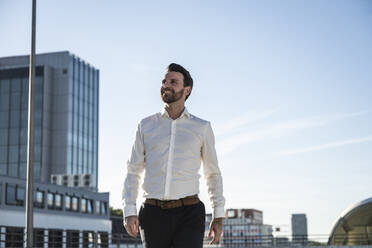 Happy businessman standing in front of sky on sunny day - UUF30464