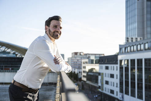 Happy businessman standing by railing on sunny day - UUF30471