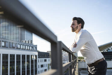 Thoughtful businessman leaning on railing in front of sky - UUF30472