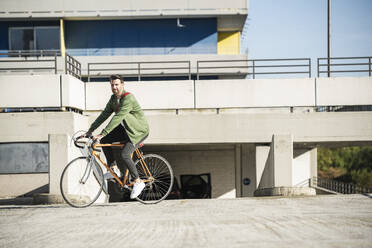 Mann fährt Fahrrad in der Nähe eines Gebäudes an einem sonnigen Tag - UUF30483