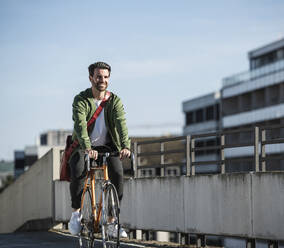 Lächelnder Mann fährt Fahrrad in der Nähe des Geländers an einem sonnigen Tag - UUF30484