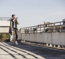 Smiling man riding bicycle and talking on mobile phone - UUF30487