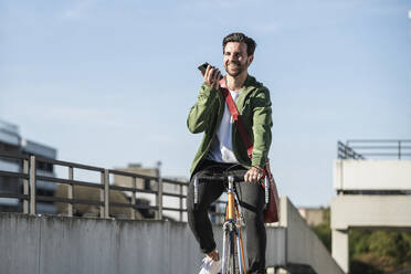 Glücklicher Mann fährt Fahrrad und spricht mit seinem Handy - UUF30488