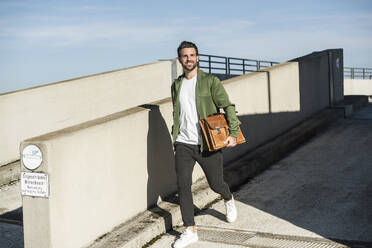 Glücklicher Mann mit Tasche an einem sonnigen Tag - UUF30496