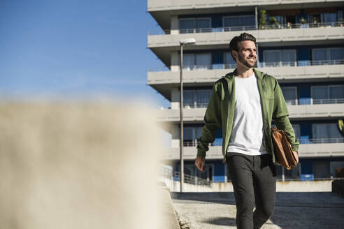 Glücklicher Mann mit Tasche vor einem Gebäude - UUF30498