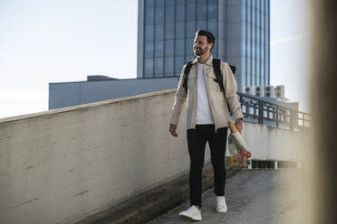 Man walking with backpack and bag of groceries in front of building - UUF30501