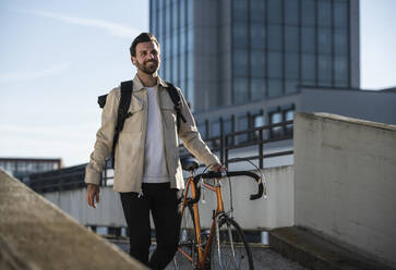 Smiling man with bicycle walking in front of building - UUF30504