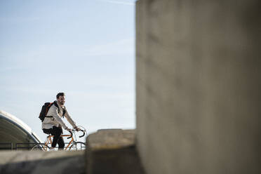 Mann mit Rucksack auf dem Fahrrad vor dem Himmel - UUF30508