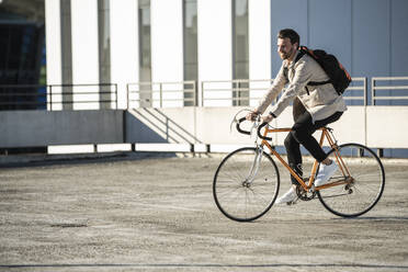 Mann mit Rucksack fährt Fahrrad auf einem Parkplatz - UUF30512