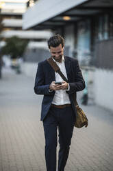 Businessman using mobile phone walking on footpath - UUF30516
