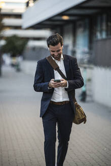 Geschäftsmann mit Mobiltelefon auf dem Gehweg - UUF30516