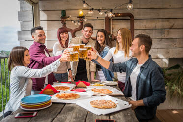 Group of happy friends bonding at home - Young adults having lunch and spending time together on a rooftop terrace, eating pizza and snacks - DMDF05558