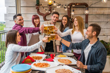 Group of happy friends bonding at home - Young adults having lunch and spending time together on a rooftop terrace, eating pizza and snacks - DMDF05559