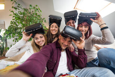Group of happy friends bonding at home - Young adults having party and playing with videogames and vr helmets - DMDF05573