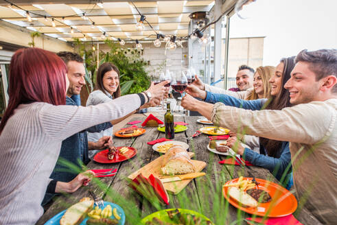 Group of happy friends bonding at home - Young adults having lunch and spending time together on a rooftop balcony, cooking meat on barbecue - DMDF05575