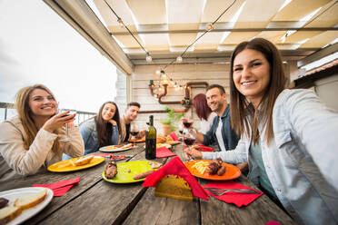 Group of happy friends bonding at home - Young adults having lunch and spending time together on a rooftop balcony, cooking meat on barbecue - DMDF05576