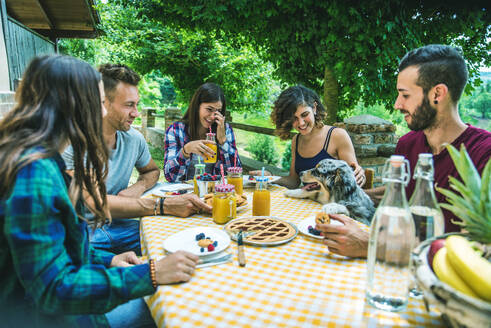 Group of happy people doing breakfast outdoors in a traditional countryside - Friends eating snacks in the garden - DMDF05716