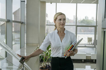 Nachdenkliche Geschäftsfrau hält Bücher und geht im Büro spazieren - OSF02165