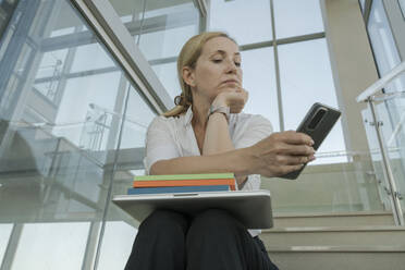 Geschäftsfrau mit Smartphone auf den Stufen im Büro sitzend - OSF02168