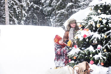 Siblings decorating Christmas tree in snow - HHF05944