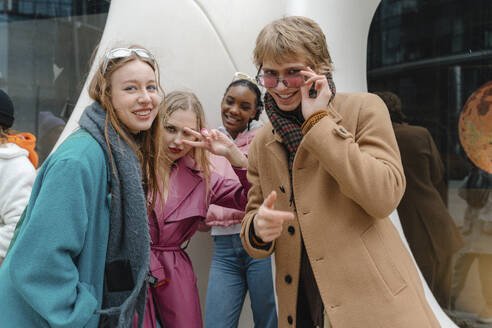 Smiling friends gesturing in front of modern building - EHAF00093