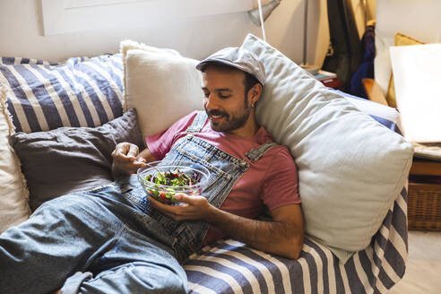 Mann isst Salat auf dem Sofa zu Hause - PCLF00708