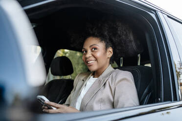 Lächelnde Geschäftsfrau hält Smartphone im Auto - MDOF01498