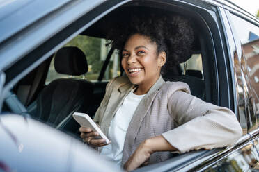 Glückliche Geschäftsfrau hält Smartphone im Auto - MDOF01499