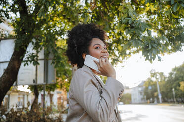 Happy businesswoman talking on smart phone near tree - MDOF01504