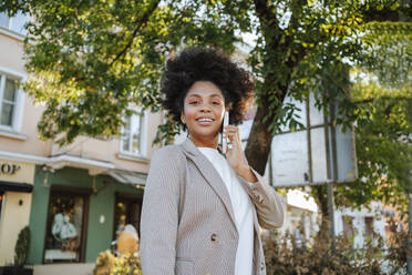 Smiling businesswoman wearing blazer talking on smart phone in city - MDOF01507